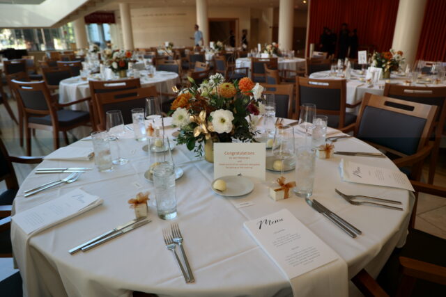 A circular table with fancy dinnerware, white tablecloth, and flower centerpiece