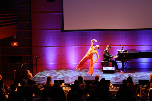 A dancer moves onstage while a pianist accompanies