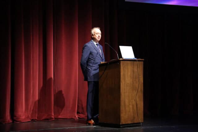 A man speaks from a lectern on stage