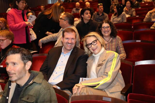 Two people smile for the camera in audience chairs